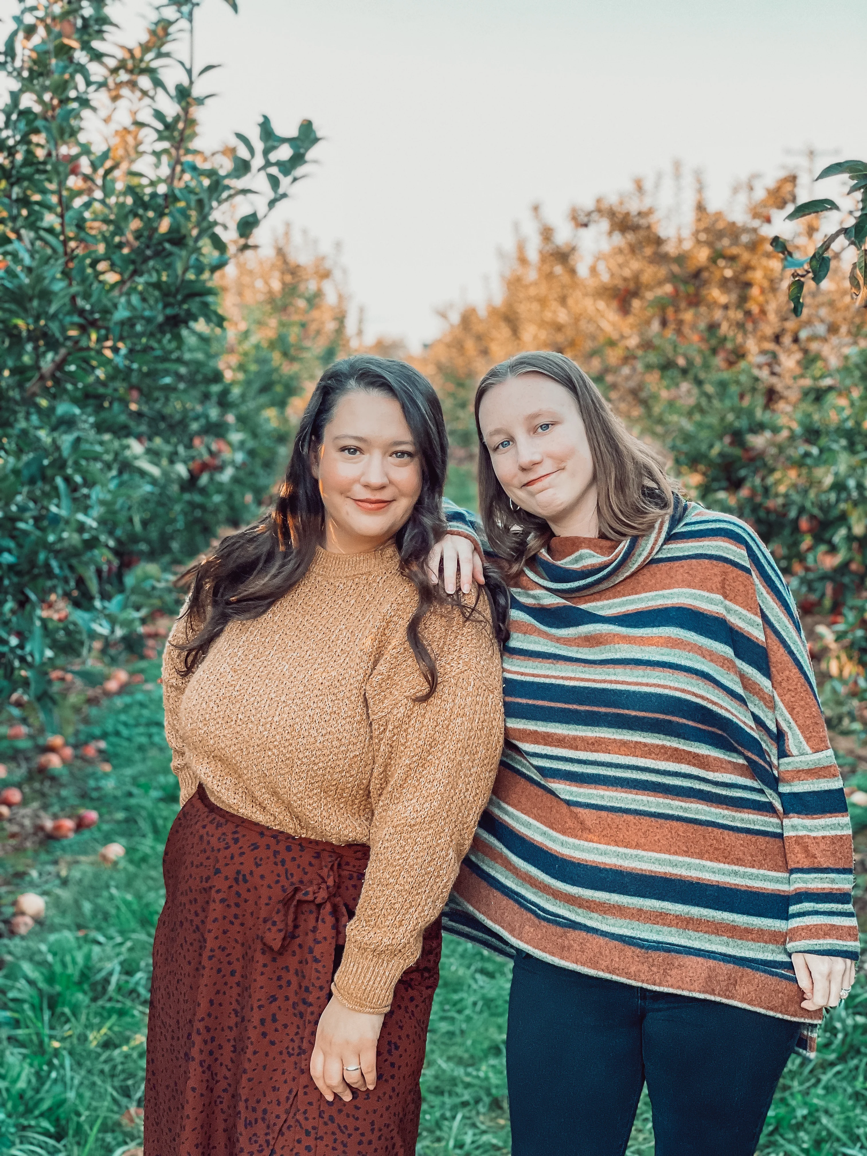 a brunette and a blonde standing in an apple orchard