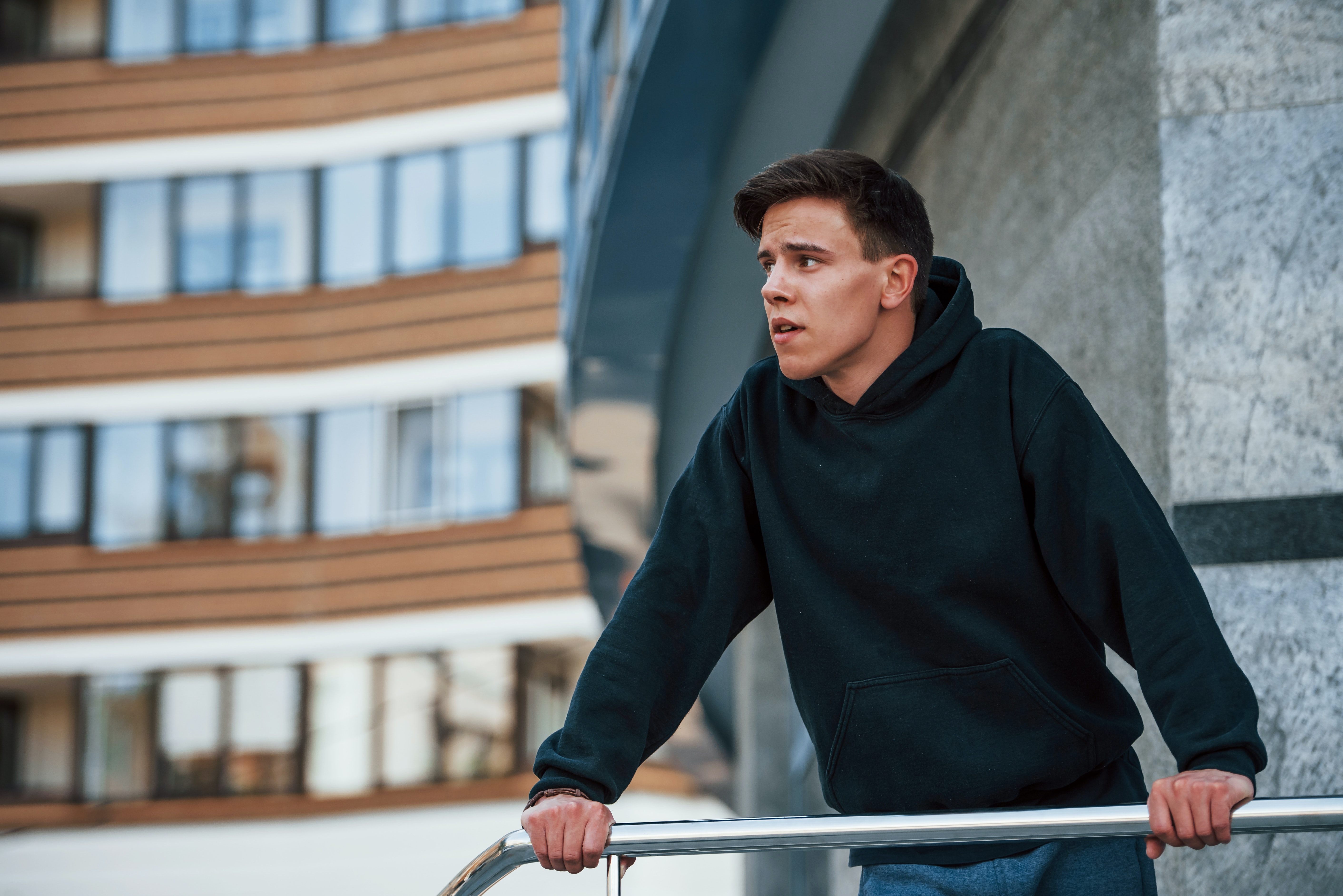 man in blue hoodie standing on a balcony looking outwards