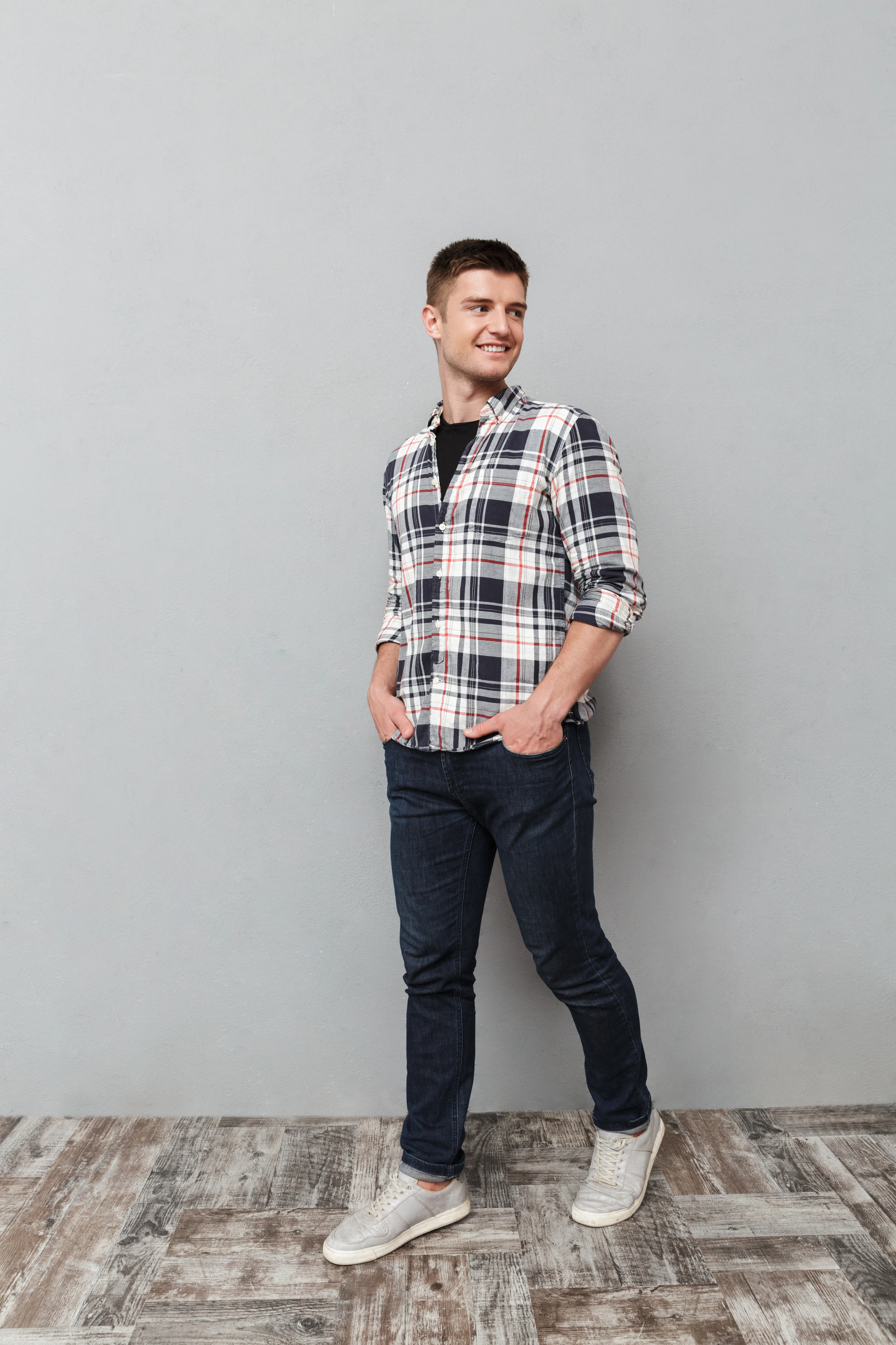 Portrait of a smiling young man in plaid shirt walking and looking away over gray background