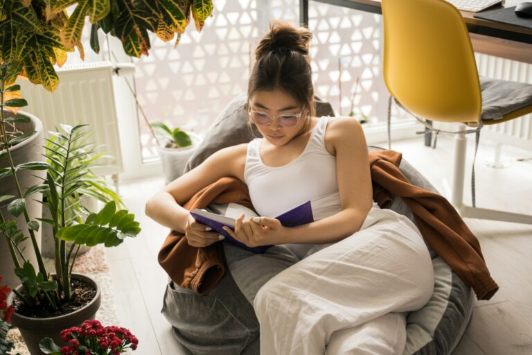 Make Self-Care in Your 30s a priority. A woman sits on a beanbag chair reading a book.