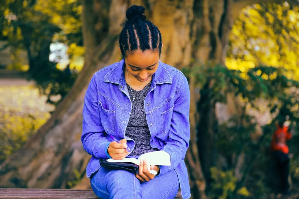 10 Thoughtful 30th Birthday Card Ideas. Woman sits writing on an bench in front of a large tree.