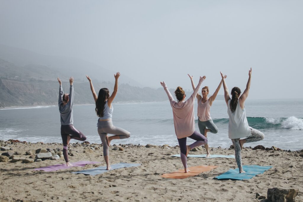 7 Striking Comparisons of Life in Your 20s vs 30sFive women doing yoga on a beach near the water.