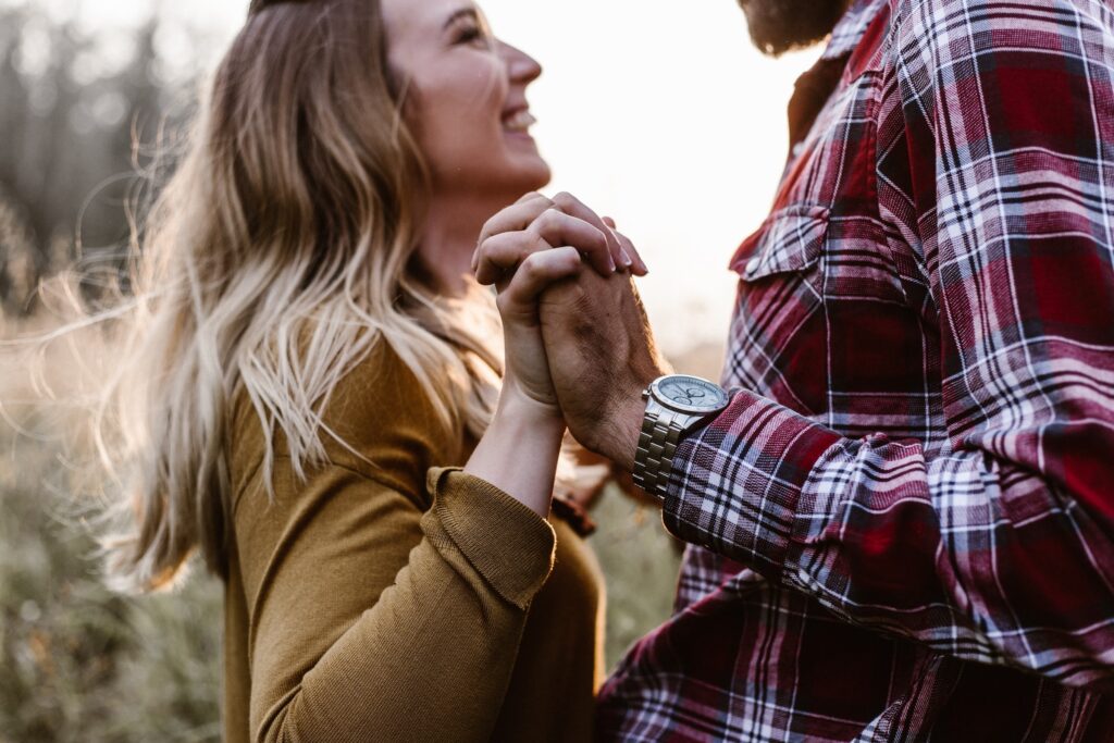 Brides Are Glad They Didn't Get Married Until Their 30s. Man and woman stand in a sunlit field facing each other, clasping hands, and smiling.